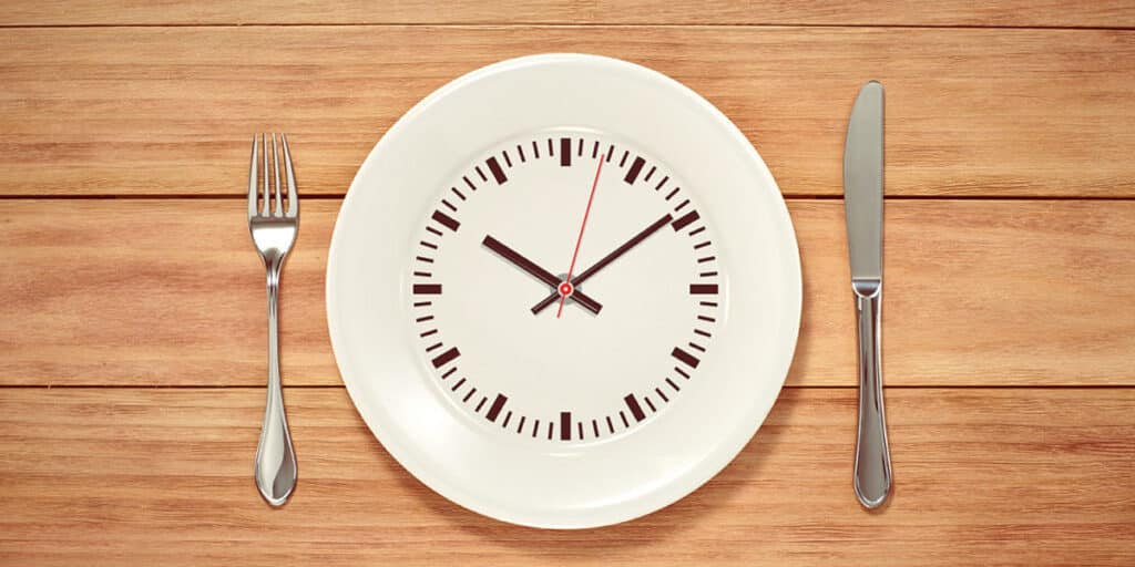 upview of a white plate simulating a clock, on a wood table and cutlery on each side