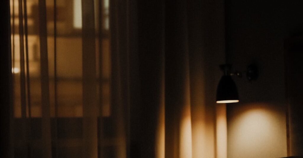 Dark, ambient hotel room with bed and soft lighting through curtains.