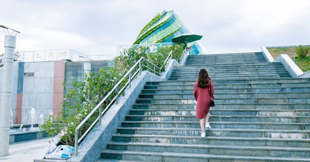 A young woman in a red dress climbs stairs towards a modern architectural structure, capturing a moment of urban exploration.